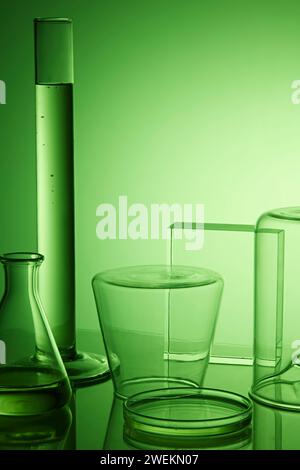 Leere Plattform für Kosmetikflaschenbehälter und wissenschaftliche Laborgeräte auf grünem Hintergrund. Laborglas mit transparenter Flüssigkeit. Fr Stockfoto