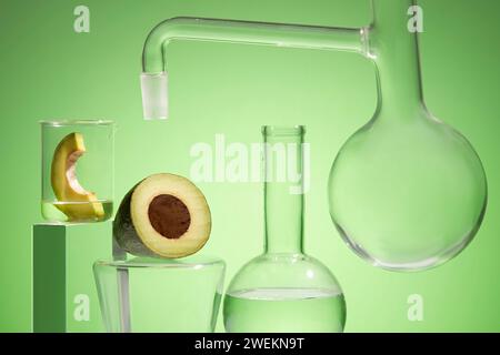 Forschungsszene kosmetischer Produkte mit Avocadoextrakt im Labor mit Laborgläsern und frischen Bio-Avocadoscheiben auf grünem Rücken Stockfoto