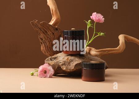 Vorderansicht von zwei Bernsteingläsern auf Stein, rosa Blumen und getrockneten Zweigen auf braunem Hintergrund. Minimales Konzept, Modell für Peeling oder Maske Produ Stockfoto