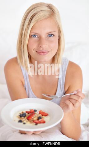 Frühstück, Porträt und Frau in einem Bett mit Müsli, Mahlzeit oder Beeren für Balance, Wellness oder Darmgesundheit zu Hause. Obst, Essen oder weibliches Gesicht Stockfoto