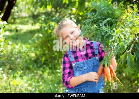 Baby Mädchen hält Karotten im Garten Kind essen gesunde Ernährung Lebensstil vegan Bio-Rohgemüse Home gewachsen Sommer Gartenarbeit Konzept Stockfoto