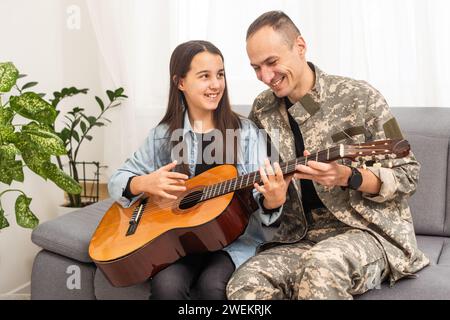 Der Veteran kam aus der Armee zurück. Ein Mann in Uniform mit seiner Tochter. Der Veteran spielt Gitarre. Stockfoto