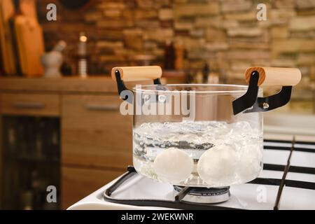 Die Eier werden in kochendem Wasser in einem transparenten Glastopf auf dem Herd gekocht Stockfoto