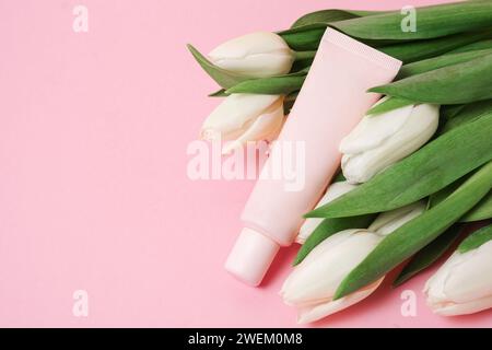 Beige Tube mit Kosmetikcreme oder Lotion für Körper und Blumenstrauß von weißen Tulpen, rosa Hintergrund, Kopierraum Stockfoto