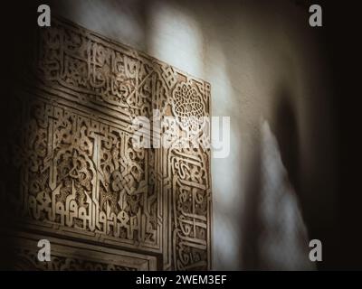 Sonnenlicht, das durch ein graviertes Fenster eines berühmten arabischen Palastes der Alhambra in Andalusien kommt, wirft Licht und Schatten auf die gravierten Wände Stockfoto