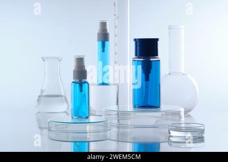 Mockup-Szene für Kosmetik mit drei blauen Sprühflaschen ohne Etikett auf transparentem Podium und Laborglaswaren gefüllt farblose Flüssigkeit dez Stockfoto