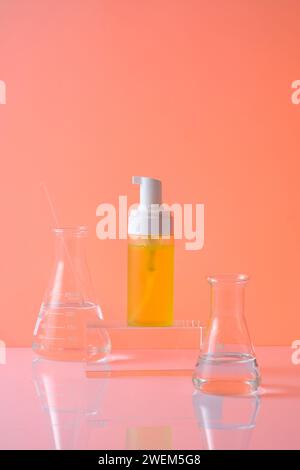 Vorderansicht des gelben Kunststoffpumpenflaschenmodells für Kosmetik auf zylindrischem, transparentem Podium und zwei erlenmeyerkolben mit Flüssigkeit, die darauf verziert sind Stockfoto
