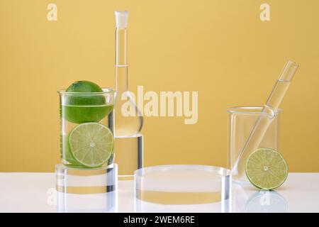 Transparentes Podium für Kosmetikprodukte, Laborgläser mit farbloser Flüssigkeit und frischen Limetten, dekoriert auf gelbem Hintergrund. Labor Stockfoto