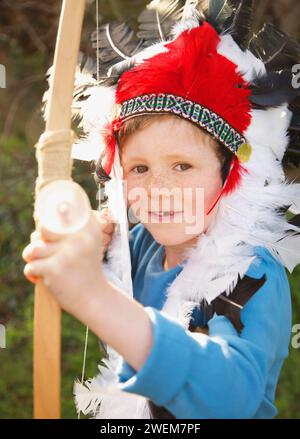 Junge mit indischem Kopfschmuck, der Bogen und Pfeil hält Stockfoto