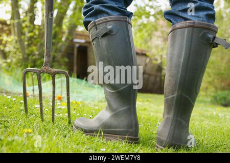 Nahaufnahme eines Mannes Beine in Gummistiefel mit Heugabel Stockfoto