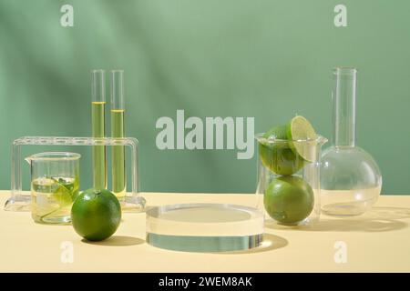Laborgeräte und Forschungsnaturextrakte aus Kalk. Transparentes Podium, frische Limetten und Laborgläser mit gelber Flüssigkeit auf grüner Rückseite Stockfoto