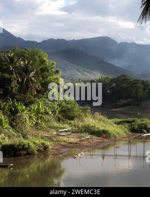 Ein Mönch überquert die Bambusbrücke während des Sonnenuntergangs in Luang Prabang Stockfoto