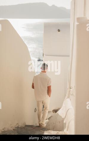 Junger Mann, der Treppen in Oia hinuntergeht und die Berge und das Meer überblickt Stockfoto