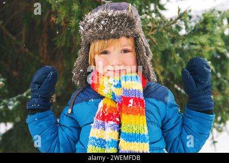 Süßer kleiner Junge, der im Winterpark spielt. Kind, das draußen Spaß hat, auf Schnee läuft, warme blaue Jacke, Hut und Schal trägt Stockfoto