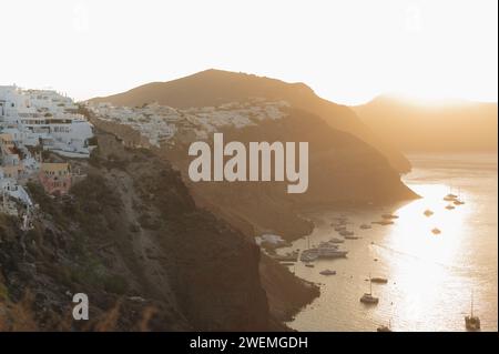 Sonnenaufgang über den Klippen von Oia mit Booten im Meer Stockfoto