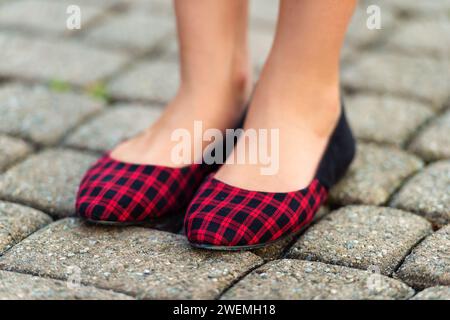 Nahaufnahme von rot-schwarz karierten Ballerinas an Kinderfüßen Stockfoto