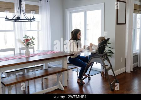 Eine Frau, die ihr Baby zum Essen bringt, während sie im Hochstuhl sitzt Stockfoto