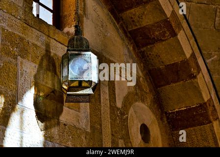 Lichtstrahl strahlte durch ein kleines Fenster im Inneren der Gemeinde Deir Al Kamar, Libanon. Auf eine bronzene Laterne, die einen Schatten auf die Wand wirft. Stockfoto