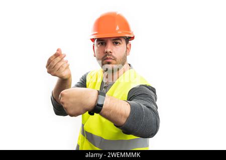 Seriöser erwachsener männlicher Baumeister in der Arbeit Uniform Weste und Helm Zeit zu machen ist Geld Geste mit Händen Fingern, die intelligente Armbanduhr als preiswertes Konzept zeigen Stockfoto