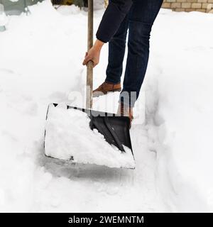 Ein Mann räumt Schnee von Pfaden auf seinem Grundstück mit einer Schaufel Stockfoto