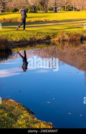 Männlicher Golfer reflektierte sich in einem Wasserteich und schlug den Golfball auf dem Fairway auf dem Golfplatz mit Mountain an einem sonnigen Tag in der Schweiz Stockfoto