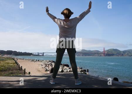 Junge Frau, die die berühmte Golden Gate Bridge über das Golden Gate in San Francisco, Kalifornien, von einem Aussichtspunkt aus betrachtet. Stockfoto