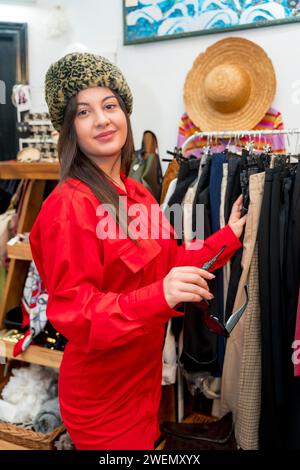 Vertikales Porträt einer Frau, die einen warmen Hut in einem Vintage-Kleiderladen anprobiert Stockfoto