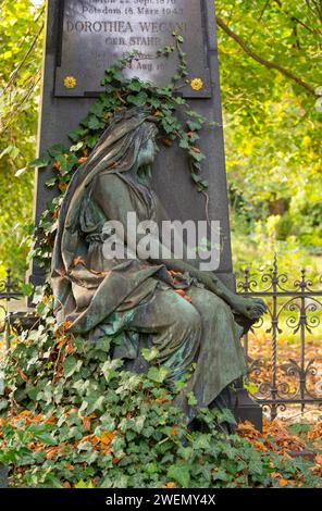 Detail einer grün patinierten Friedhofsskulptur umgeben von Efeu und Bäumen, Herbstblätter, Skulptur einer trauernden Frau mit grüner Patina in A Stockfoto