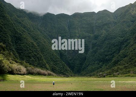 Ein Wanderer steht im trockenen Grand Etang, auf der Insel Réunion, mit majestätischen Bergen im Hintergrund. Stockfoto