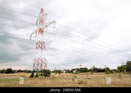 Ein hoch aufragender Strompylon steht vor einem bewölkten Himmel, mit mehreren Hochspannungsleitungen, die sich über eine ländliche Landschaft erstrecken. Stockfoto