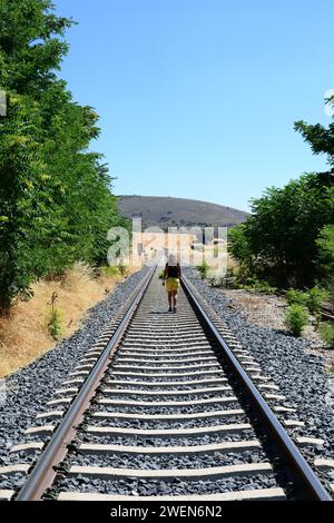 Eine junge Frau läuft nachdenklich entlang der Bahngleise durch die Landschaft Stockfoto