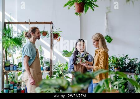 Gastfreundliche kaukasische männliche und asiatische Geschäftsinhaberinnen, die mit einem Kunden in einem Blumenladen chatten. Stockfoto