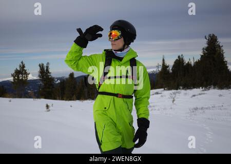 Mann in hellsäuregrünem Snowboardanzug, schwarzen warmen Handschuhen, orangen Brillen, Helm und Rucksack Skier Outfit, reicht Hand in Richtung seines Hades. Erkundet s Stockfoto