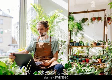 Der gutaussehende kaukasische Mann Besitzer eines Blumengeschäfts in kleinen Unternehmen, der Technologie zur Optimierung täglicher Aufgaben im Blumengeschäft verwendet, nutzt den Computer bequem an Stockfoto