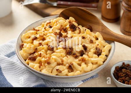 Makkaroni und Käse mit Speckstücken in einer weißen Servierschale und Holzlöffel Stockfoto