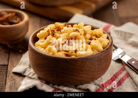 Makkaroni und Käse mit Speckstücken in einer Holzschale auf einem Handtuch und rustikalem Holztisch Stockfoto