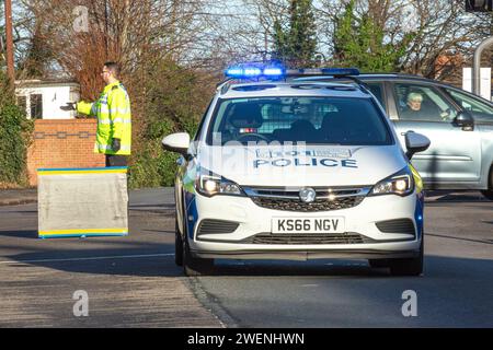 Verkehrsereignis in Großbritannien: Vorderansicht des Polizeiautos von West Mercia mit blinkenden blauen Lichtern und männlicher Polizist, der den Verkehr hinter dem Fahrzeug auf der Straße lenkt. Stockfoto