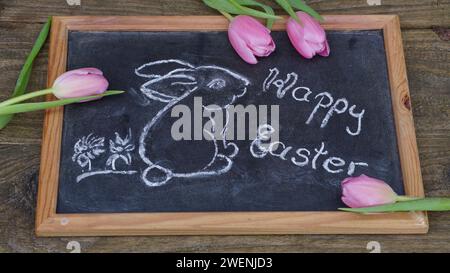 Ein osterhase und frohe ostern auf der Tafel. Pinkfarbene Tulpen. Stockfoto