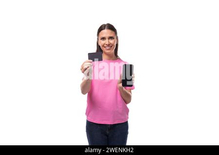 Junge schlanke Frau in einem rosa Baumwoll-T-Shirt mit Kreditkarte und Smartphone Stockfoto