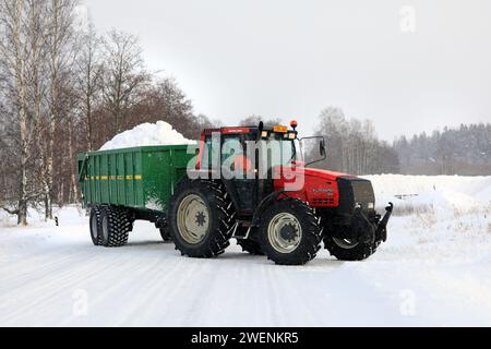 Der rote Valtra Valmet 8550-Traktor transportiert die Schneeladung des Anhängers von der Straße in die kommunale Schneemängelzone. Salo, Finnland. Januar 2024. Stockfoto