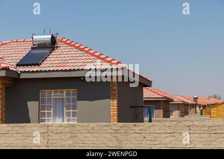 Eine neue Wohnunterteilung mit solarbetriebenen Warmwasserbereitern auf den Dächern in Mogwase, Nordwesten, Südafrika. Stockfoto