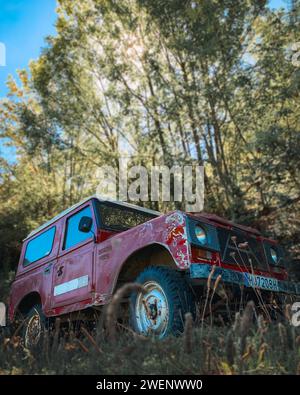 Ein alter alter roter Geländewagen, der an einem sonnigen Tag mitten im Wald der Pyrenäen geparkt wurde Stockfoto