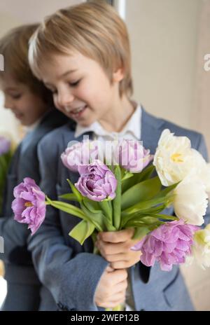 Junge von 6-7 Jahren steht neben dem Spiegel, hält einen Tulpenstrauß in der Hand, lächelt träumend Stockfoto