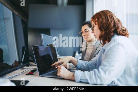 Eine vielfältige Gruppe von Fachleuten diskutiert und arbeitet in einem modernen Büro zusammen. Sie arbeiten auf Laptops und konzentrieren sich auf Software-Design und -Programmierung. Mit t Stockfoto