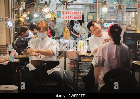 Taipeh, Republik China - 1. Oktober 2023: Eine Frau erhält in der geschäftigen und geschäftigen Raohe Street ein traditionelles Gesichtsfäden zur Haarentfernung Stockfoto