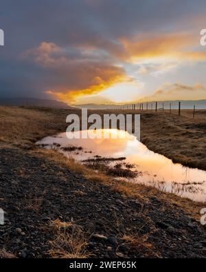 Wasser fließt über Felsen in der Nähe eines Zauns, umgeben von üppiger Vegetation Stockfoto