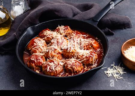 Rindfleischbällchen mit Grilltomatensoße und Parmesankäse in gusseiserner Pfanne auf grauem Hintergrund, Nahaufnahme Stockfoto