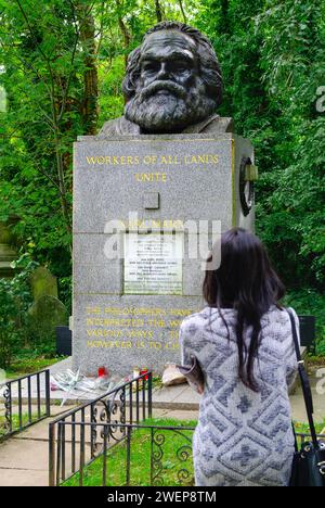 London: Am Grab von Karl Marx. - Eine junge Frau steht auf dem Highgate-Friedhof in London mit erhobener Faust neben der gepflegten Grabstätte von Kar Stockfoto