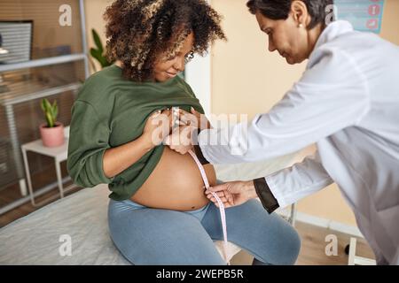 Geburtshelfer zur Kontrolle des Abdomens der Schwangeren mit dem Maßband Stockfoto