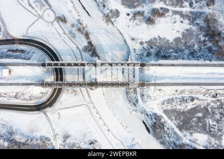 Blick von oben auf die Eisenbahnbrücke über den gefrorenen Fluss mit Schnee an einem sonnigen Wintertag. Stockfoto